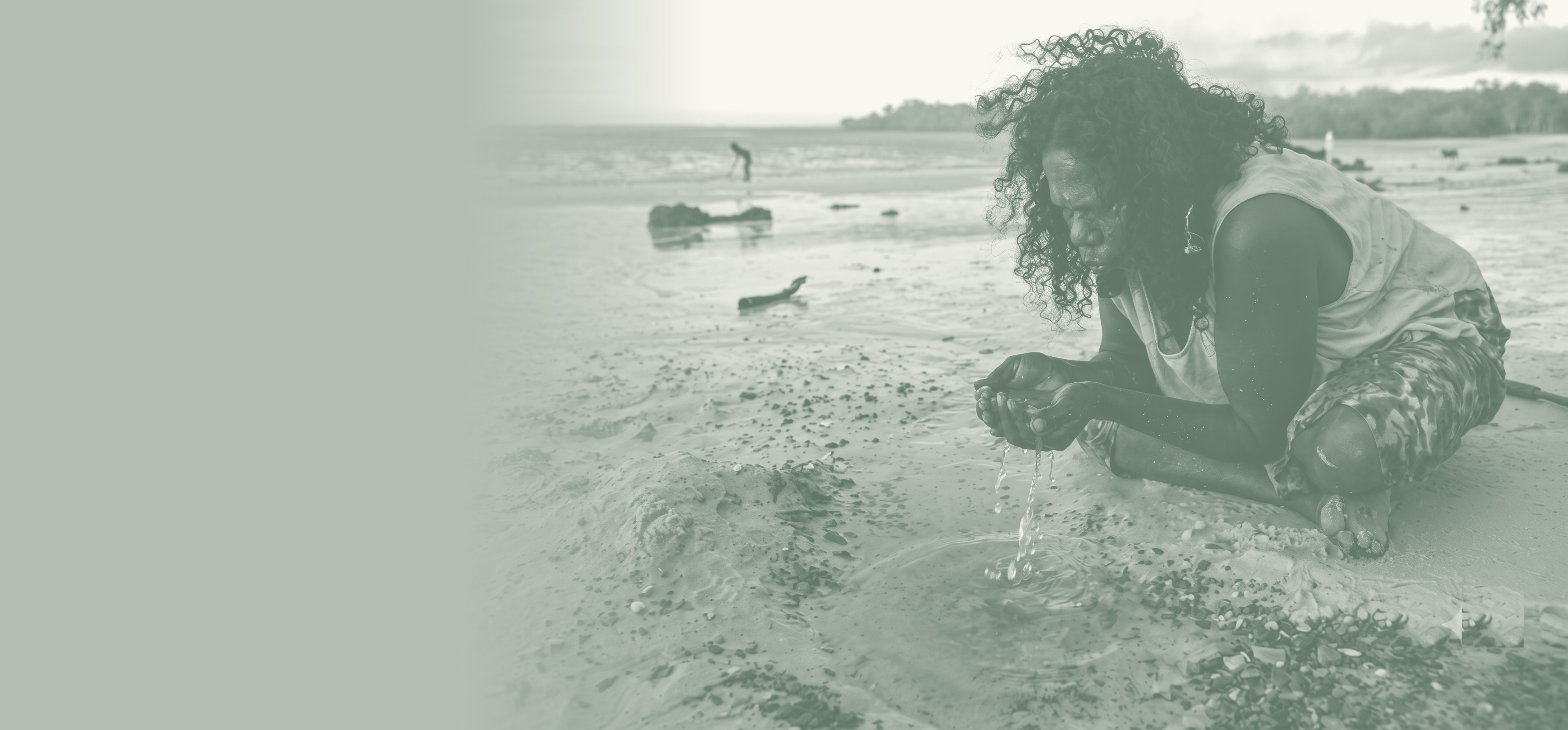 An Aboriginal woman drinking fresh water gathered from the land at the water's edge